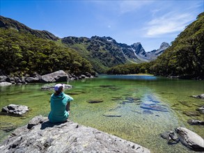 Rear view of woman sitting on lakeshore in Fiordland National Park, Te Anau, Fiordland, New Zealand