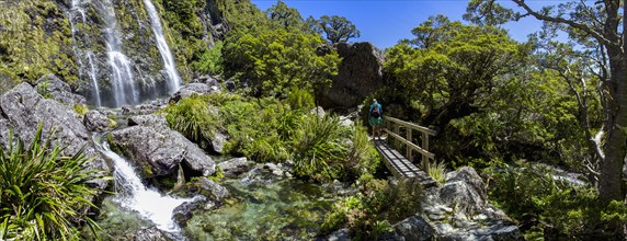 Rear view of hiker crossing footbridge near waterfall in Fiordland National Park, Te Anau,