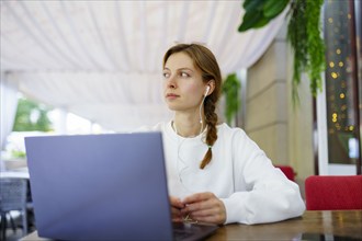 Woman with headphones using laptop at cafe table, Omsk, , Russia