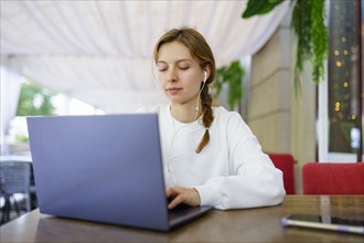 Woman with headphones using laptop at cafe table, Omsk, , Russia