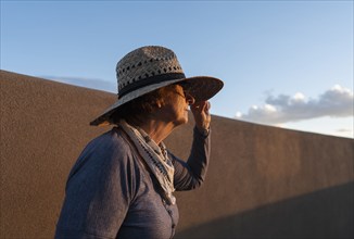 Usa, New Mexico, Santa Fe, Woman in straw hat standing against adobe wall in High Desert, Santa Fe,