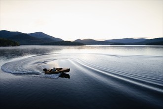 USA, New York, Lake Placid, Man in wooden boat on lake at sunrise, Lake Placid, New York, USA