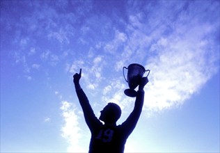 Silhouette of man holding up trophy against sky, Mendham, New Jersey, USA