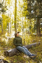 USA, New Mexico, Pensive boy sitting on log in Santa Fe National Forest, Santa Fe, New Mexico, USA