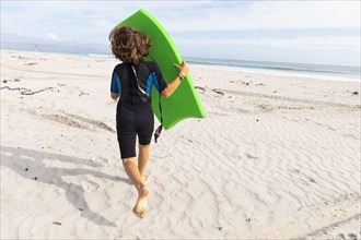 South Africa, Hermanus, Rear view of boy running on beach with body board, Hermanus, , South Africa