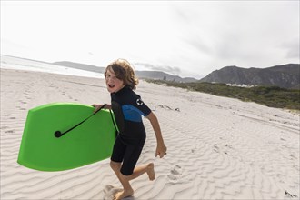 South Africa, Hermanus, Smiling boy running on beach with body board, Hermanus, , South Africa