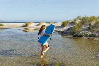 South Africa, Hermanus, Teenage girl walking on beach with body board, Hermanus, , South Africa