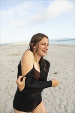 South Africa, Hermanus, Teenage girl putting on wetsuit on beach, Hermanus, , South Africa