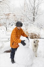 Boy with his dog building snowman, Santa Fe, New Mexico, USA