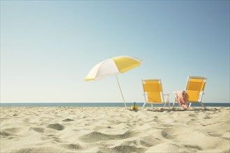 USA, Massachusetts, Nantucket, Two yellow beach chairs and umbrella on sandy beach facing ocean,