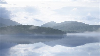 USA, New York, Lake Placid, Calm Lake Placid reflecting hills and clouds, Lake Placid, New York,