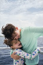 Brother (10-11) and sister (6-7) hugging on boat, , St. John, US Virgin Islands