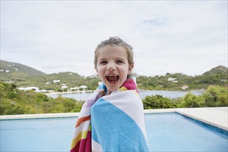 Portrait of smiling girl (6-7) wrapped in towel by swimming pool, , St. John, US Virgin Islands