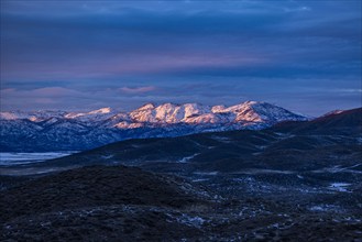 Sunset light on distant snowy mountains outside Mountain Home, Mountain Home, Idaho, USA