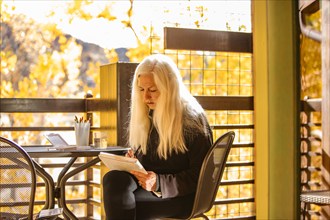 Woman with long white hair painting watercolors on deck in autumn, Springdale, Utah, USA