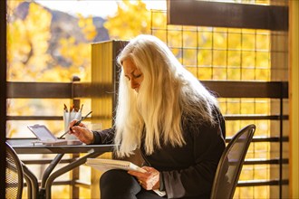 Woman with long white hair painting watercolors on deck in autumn, Springdale, Utah, USA