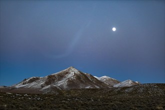 Full moon over snow covered hills at dusk, Wells, Nevada, USA