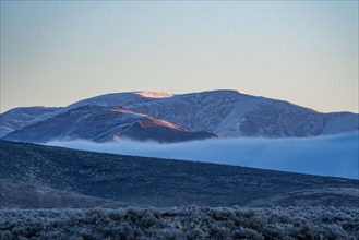 Low hanging cloud in fold between foothills covered with frost at sunrise, Picabo, Idaho, USA