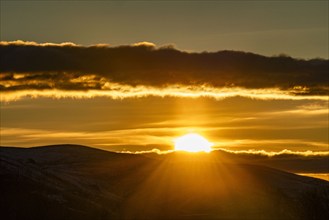 Clouds above golden sun setting behind hills, Bellevue, Idaho, USA