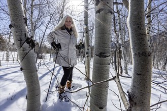 Smiling woman snowshoeing through aspen forest, Sun Valley, Idaho, USA