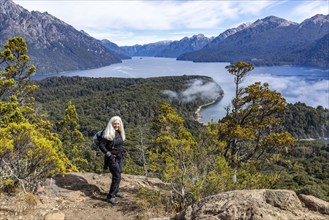 Smiling woman with long white hair standing on top of hill above mountain lakes, Bariloche, ,