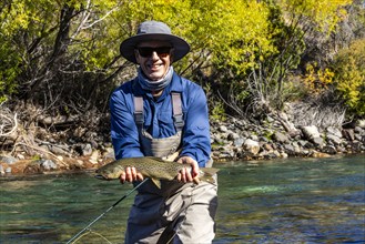 Portrait of smiling fly-fisherman holding native brown trout from Traful River before releasing it