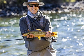 Portrait of smiling fly-fisherman holding native brown trout from Traful River before releasing it