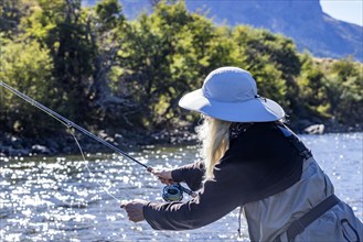 Woman in white hat fly fishing on Traful River on sunny day, Estancia Arroyo Verde, Nequen