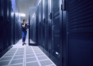 Female technician using laptop and phone in server room 
St, George, Utah, USA