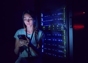 Female technician looking at smart phone in server room 
St, George, Utah, USA