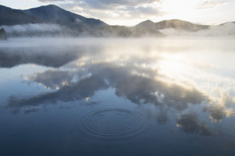 Morning mist over calm Lake Placid surface reflecting clouds and sunlight
Lake Placid, New York