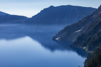 USA, Oregon, Hills reflected in calm, blue Crater lake
