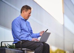 Man working on laptop and looking at phone outdoors