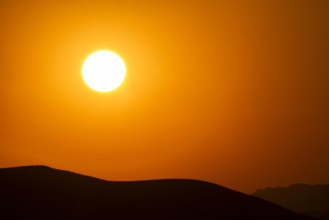 USA, Idaho, Bellevue, Setting sun over hills against orange sky