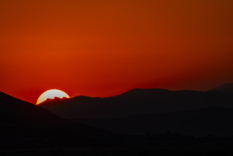 Sun setting behind hills against orange sky