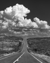 USA, Idaho, Fairfield, Cumulus clouds over empty road crossing landscape, black and white