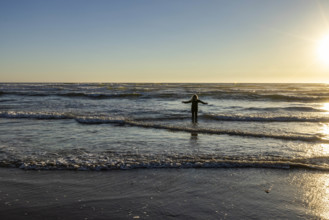 USA, Oregon, Cannon Beach, Woman wading in surf at sunset