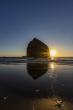 USA, Oregon, Sun setting behind haystack rock on Cannon Beach