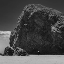 USA, Oregon, Brookings, Rear view of woman walking by huge rocks on Oregon beach, black and white