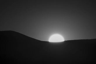 USA, Idaho, Bellevue, Sun setting behind hill, black and white