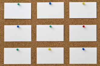 Blank pieces of paper attached to cork board with colorful push pins
