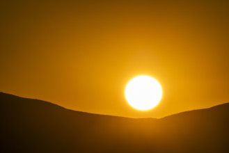 Sun setting over hills against orange sky