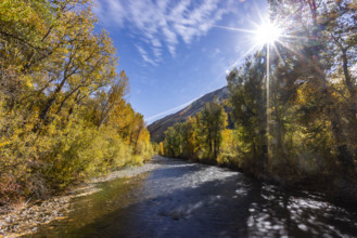USA, Idaho, Hailey, Big Wood River and sun shining through trees with fall foliage