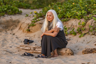 Senior woman sitting on beach at sunset