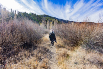 USA, Idaho, Sun Valley, Rear view of woman in wool poncho on footpath in landscape