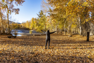 USA, Idaho, Bellevue, Rear view of woman standing with arms raised near Big Wood River in autumn