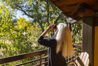 Senior blonde woman using binoculars on porch in autumn