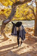 USA, Utah, Zion National Park, Woman in poncho and hat standing by tree along Virgin River