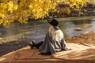 USA, Utah, Zion National Park, Rear view of woman in poncho and hat sitting by Virgin River