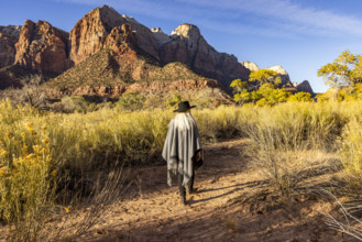 USA, Utah, Zion National Park, Rear view of woman in poncho and hat walking near Virgin River
